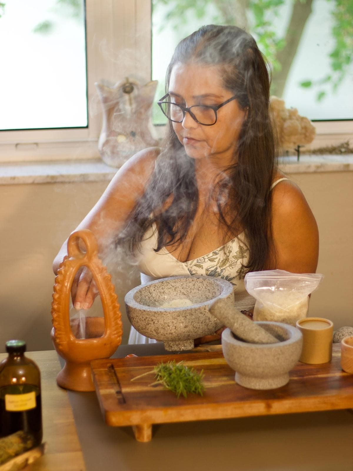 Leslie preparing botanicals, copal smoke, stone mortar and fresh herbs